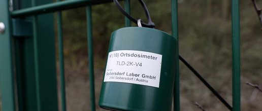 Anbringung eines Umgebungsdosimeters mittels Kabelbinders an einem Zaun.